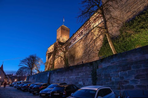 Nuremberg Kaiserburg in evening lighting, blue evening sky, cars parked below on the castle wall,