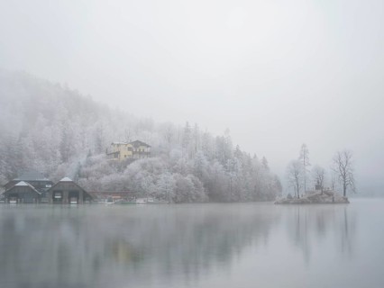 View across Königssee to boathouses, Christlieger island and frozen trees in fog, Schönau am