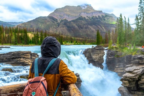 Tourist wearing a backpack and hooded jacket admiring the breathtaking view of powerful athabasca