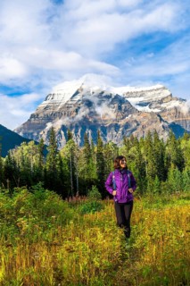 Female hiker walking through a meadow enjoying the view of mount robson on a sunny day with clouds