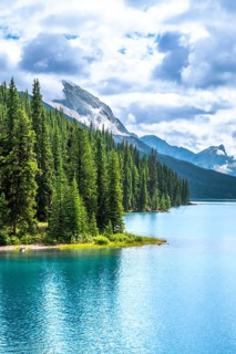 Turquoise maligne lake reflecting a cloudy sky, surrounded by lush pine forests and rocky mountains