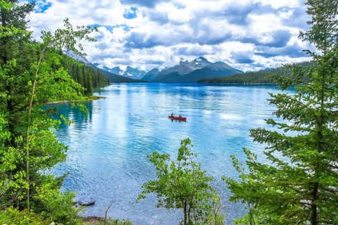 Two tourists enjoying a canoe ride on the turquoise waters of maligne lake, surrounded by lush