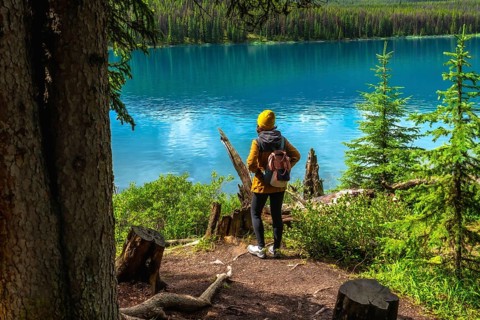 Female hiker admiring the stunning turquoise waters of maligne lake, surrounded by lush forests in
