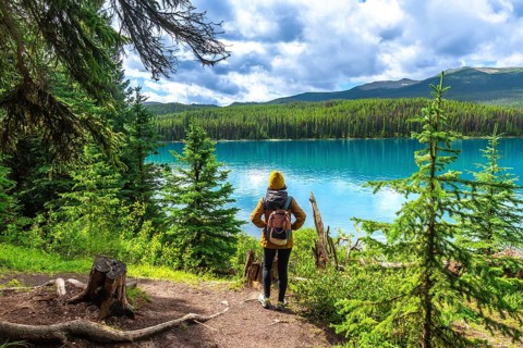 Female hiker with a backpack admiring the stunning turquoise waters of maligne lake, surrounded by
