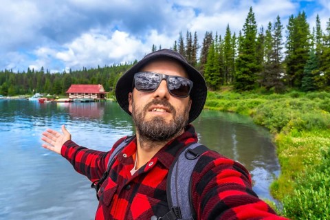 Happy tourist showing with open arms the beautiful maligne lake with the boathouse at jasper