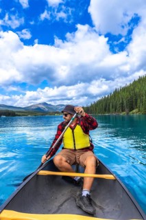 Tourist wearing sunglasses and life jacket paddling a canoe on beautiful maligne lake in jasper