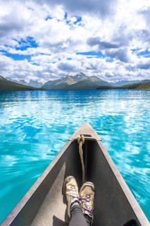 Tourist enjoys stunning view of turquoise water and mountain range while paddling canoe on maligne