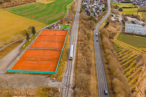 Aerial view of a landscape with railway tracks, tennis courts and roads, surrounded by fields and