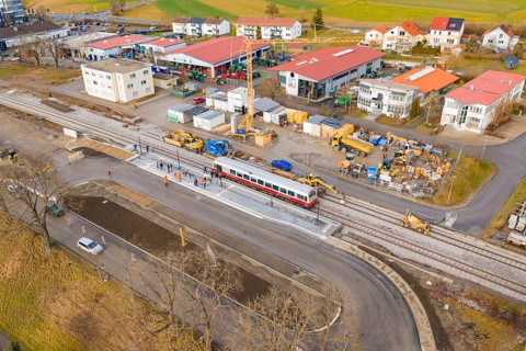 Workers and machines are working on an extensive construction site near tracks and a passing train,