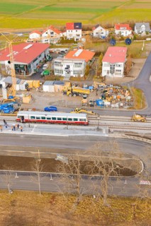 A train passes a construction site with numerous buildings and a crane in a rural area, historic