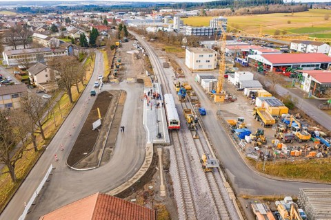 A few houses and a construction site at a municipal train station with train and construction work,
