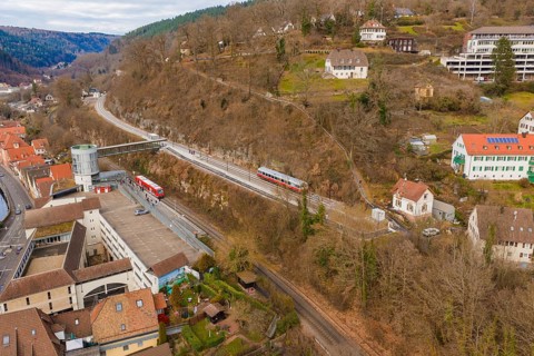 Zug crosses an urban landscape with hilly terrain and houses under a cloudy sky, historic event,