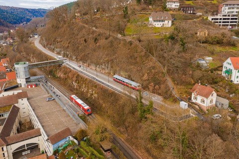 Two trains travel through an urban area with hills and buildings, surrounded by winter vegetation,