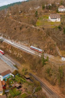 Train travels through hilly terrain with buildings and trees in a winter environment, historic
