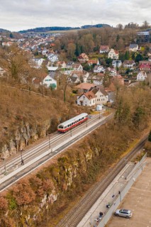 A train passes by a mountain range. In the background is a small town with many houses, historic