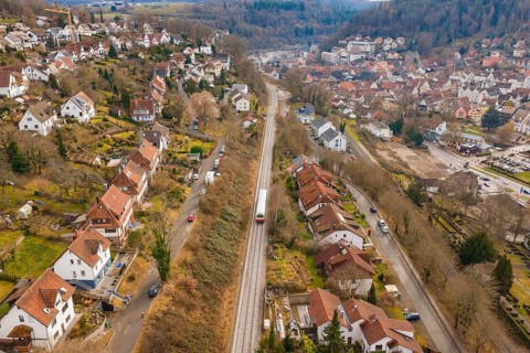 A train travels through a residential area that stretches along a wooded hill, historic event,