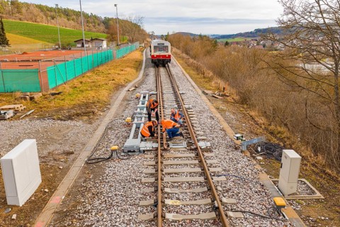 Construction workers working on railroad tracks with a train standing in the background, historic