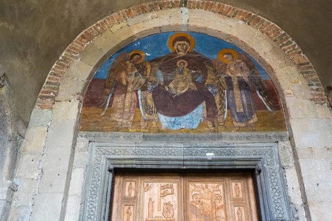 Fresco depicting Mary and Child Jesus and angels in a round arch above a decorated door,