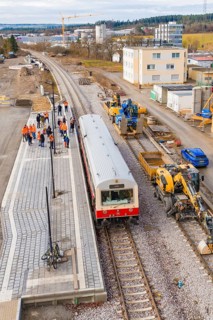Train stops at a construction site surrounded by workers with industrial buildings in the