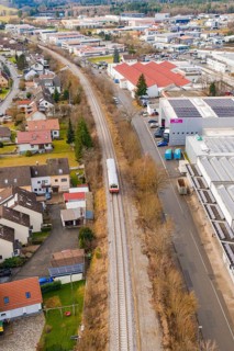 Train travels through a suburb with residential buildings and industrial buildings, surrounded by