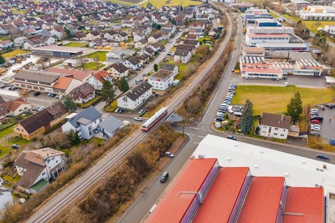 Train travels in a suburban landscape between residential buildings and industrial buildings,
