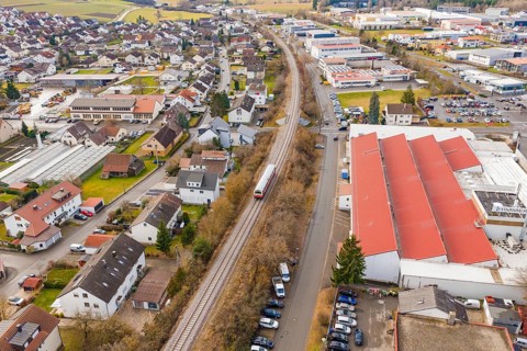 Train on rails in a suburb with residential buildings and industrial facilities, surrounded by