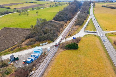 A rural scene with a train on rails, surrounded by fields and roads, historic event, first test run