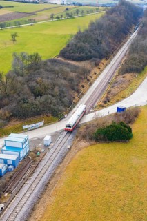 Train travels through a rural landscape with small infrastructures and surrounded by fields,