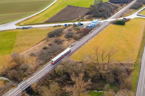 A train on rails crosses a rural landscape with fields and hills, historic event, first test run
