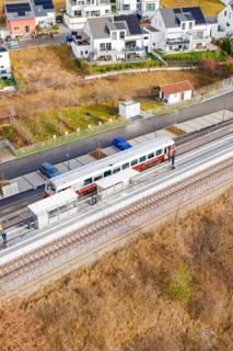 Train on the platform, surrounded by residential buildings and parked cars, historic event, first