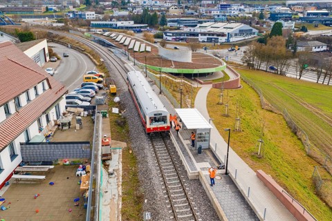 A train stops at a train station in an urban area, surrounded by buildings and parking lots,