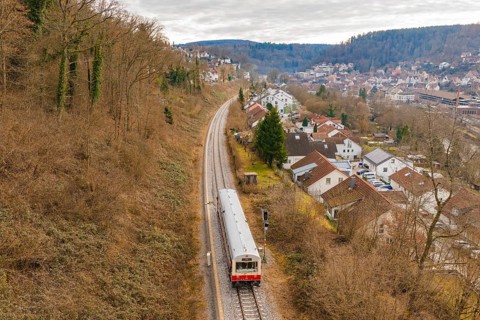 A train moves through a picturesque landscape with houses and hills in the background, historic
