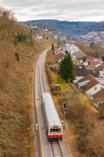 A train travels through a hilly landscape with houses and autumn trees, historical event, first