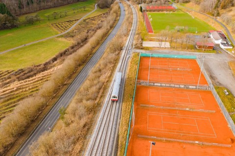 Train travels along tennis courts and green areas, autumn landscape with road and trees in the