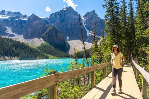 Female tourist walking along a wooden path, admiring the stunning turquoise waters of moraine lake
