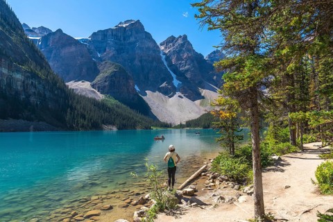 Female tourist standing on the shore of the turquoise moraine lake, admiring the canadian rockies