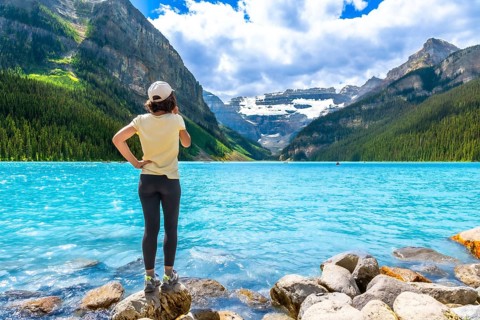 Tourist standing on rocks at the edge of vibrant turquoise waters of lake louise, admiring majestic