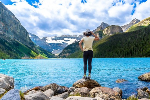 Tourist standing on rocks by the turquoise water of lake louise admires the surrounding canadian