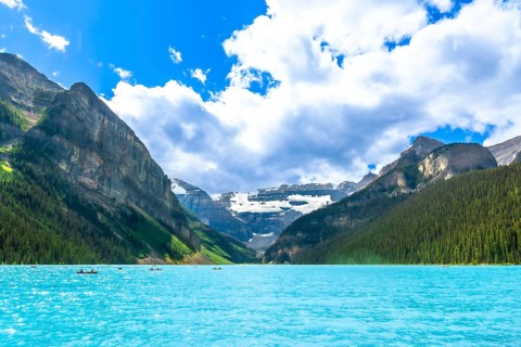 Canoes are paddling on a beautiful turquoise lake with surrounding mountains and glaciers in banff