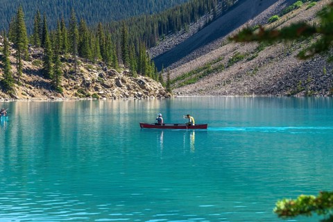 Two tourists paddling a red canoe on the turquoise waters of moraine lake in banff national park,