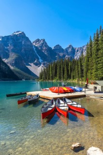 Colorful canoes are waiting at a wooden dock on the turquoise, pristine waters of moraine lake in