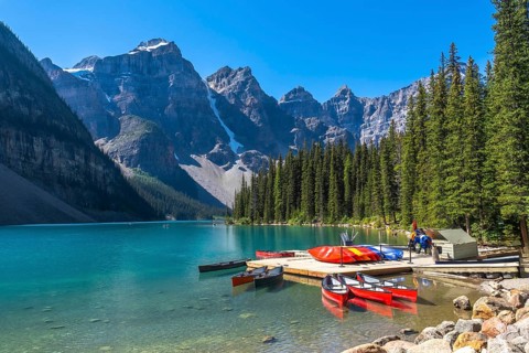 Colorful canoes tied to a wooden dock on turquoise waters of moraine lake, surrounded by the