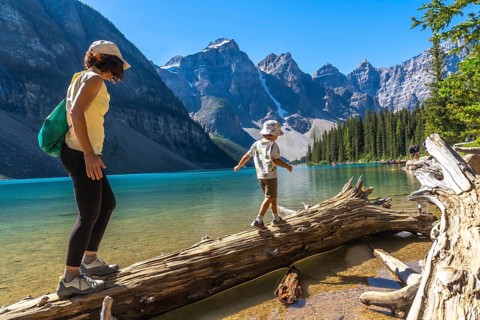 Mother and son balancing on a weathered log over turquoise waters of moraine lake, surrounded by