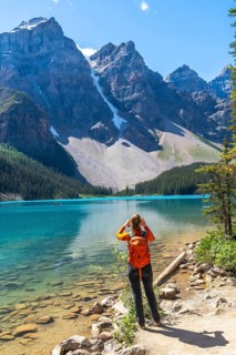 Female tourist with backpack taking pictures of the turquoise waters of moraine lake and the