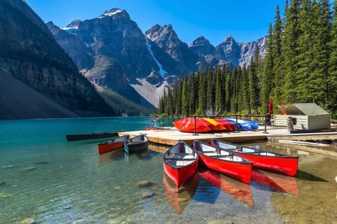 Reflecting red canoes in the turquoise waters of moraine lake, framed by snow capped mountains and