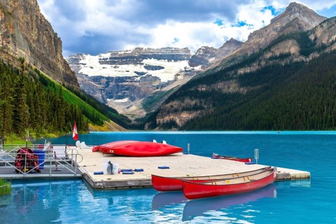 Red canoes are tied to a dock on the turquoise water of lake louise with a backdrop of snow capped