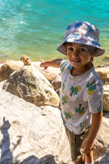 Young tourist pointing at a golden mantled ground squirrel on a rock by the turquoise waters of