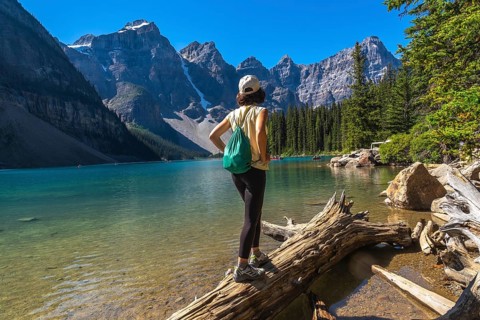 Female tourist standing on a log and admiring the turquoise waters of moraine lake, framed by the