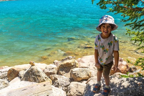 Happy child wearing a bucket hat standing by the turquoise water of moraine lake with a chipmunk