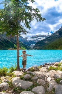 Young tourist with arms outstretched, enjoying the stunning turquoise waters of lake louise and the
